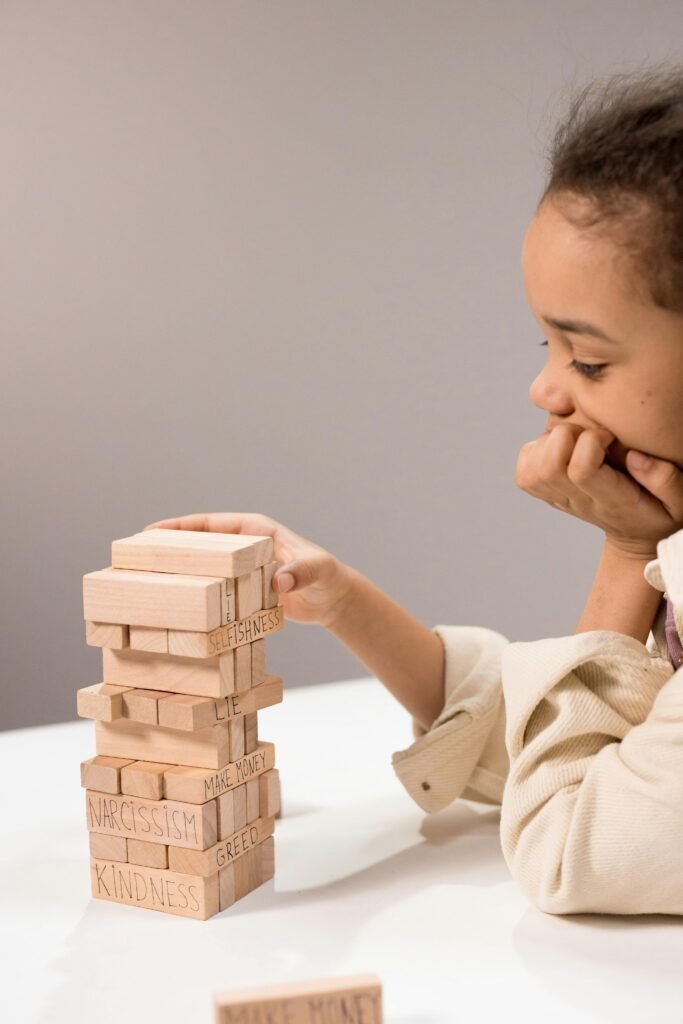A young girl concentrates on a Jenga game with words like 'Kindness' and 'Narcissism' on blocks.